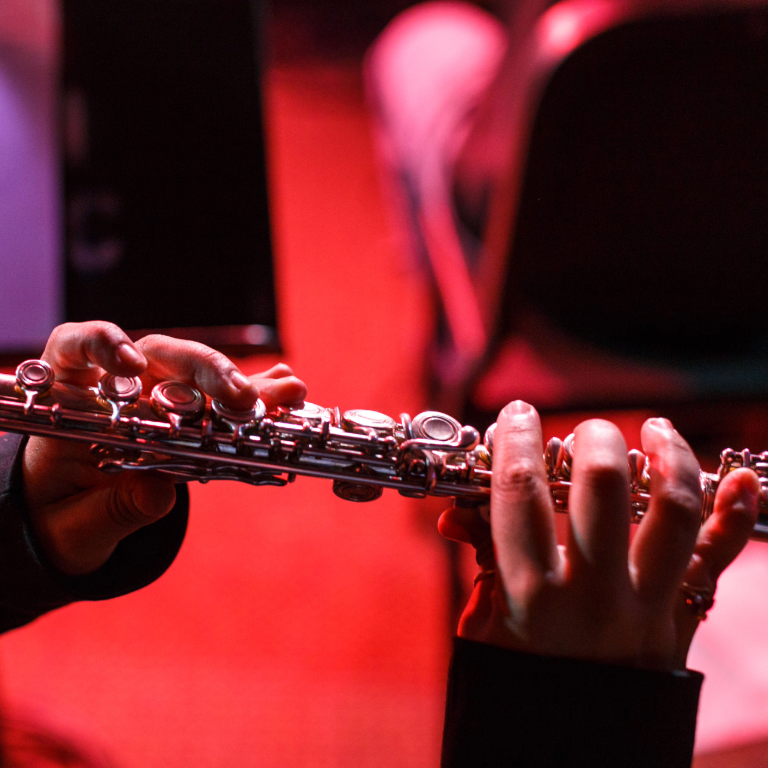 Color photograph of a pair of hands playing a flute onstage during a Music and Arts Technology ensemble performance.