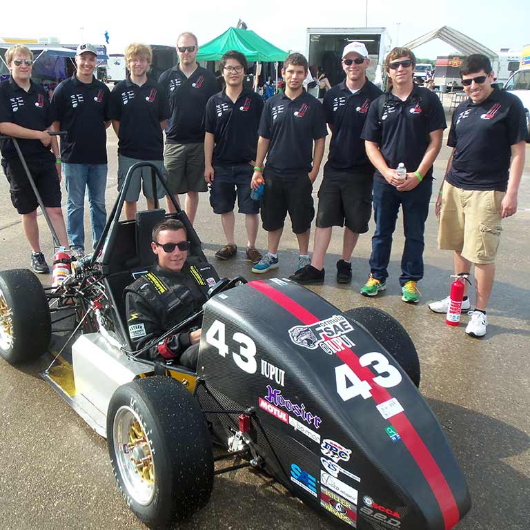 Furniture design students gather around a race car.