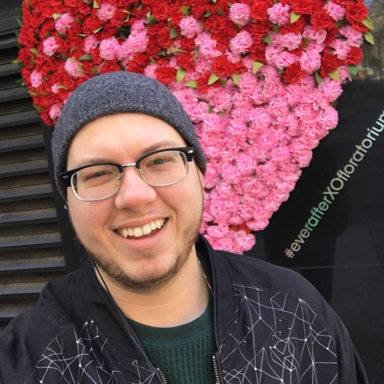 Keaton Evans-Black posing in front of a colorful heart-shaped flower arrangement.