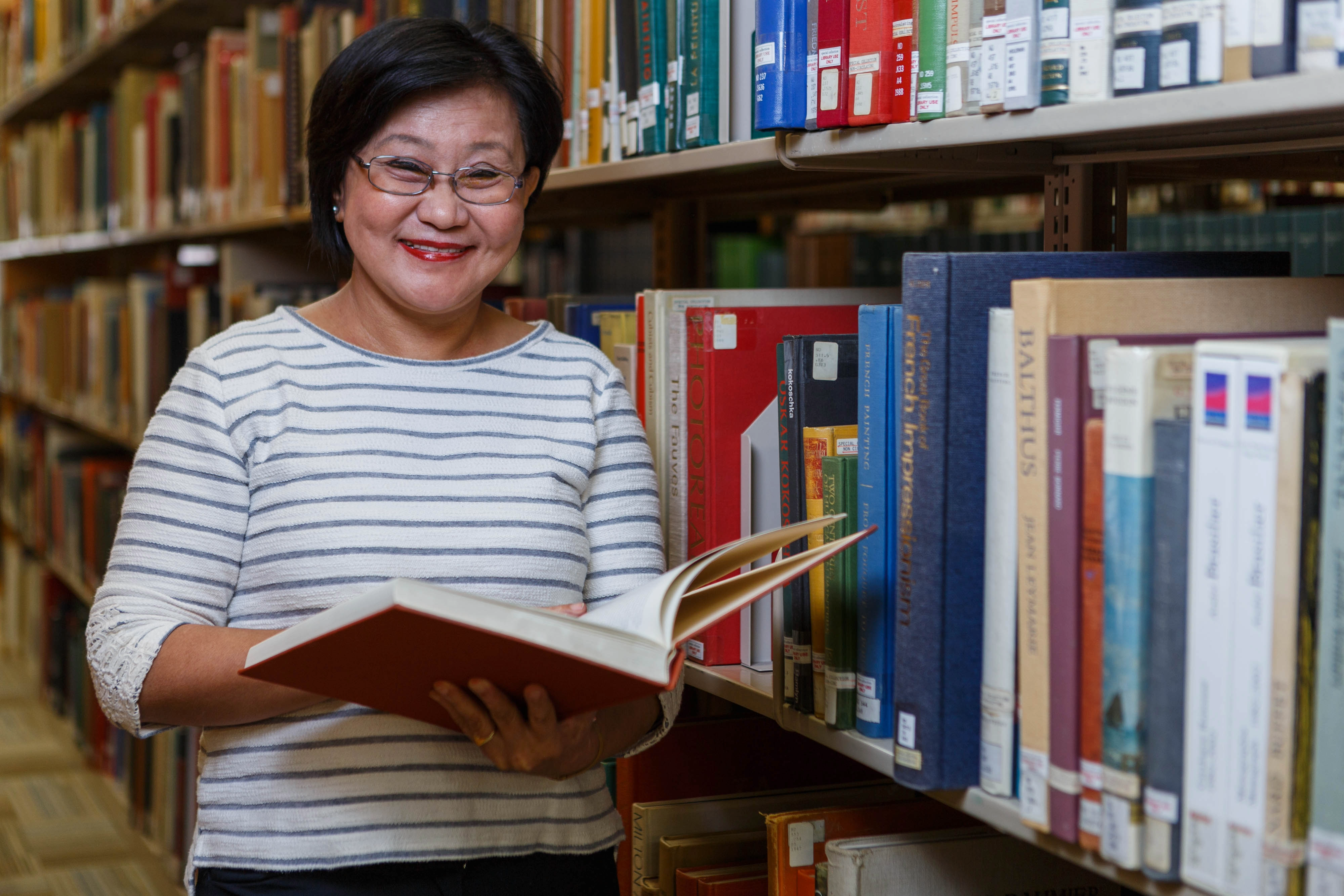 Art history professor Uranchimeg Tsultem smiles while holding an art book open in the stacks at Herron's art library
